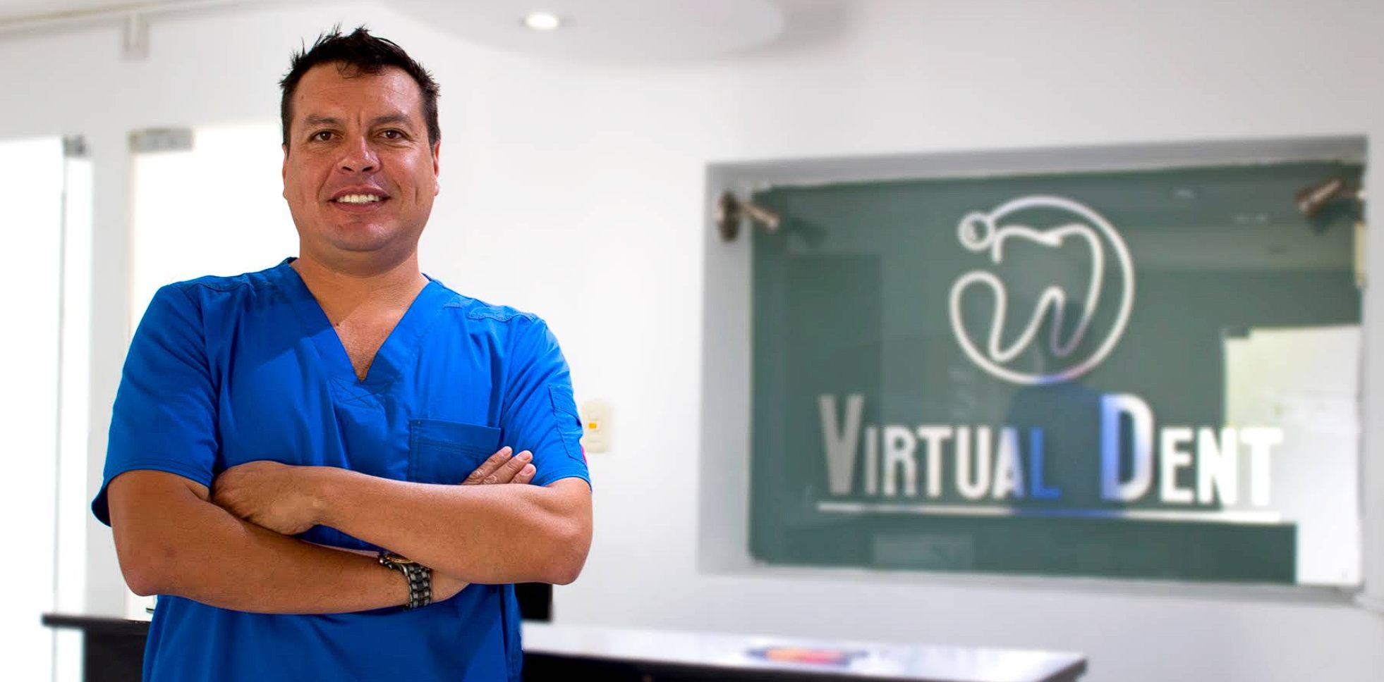 Odontólogo de Virtual Dent con uniforme azul en la recepción, junto al letrero de la clínica