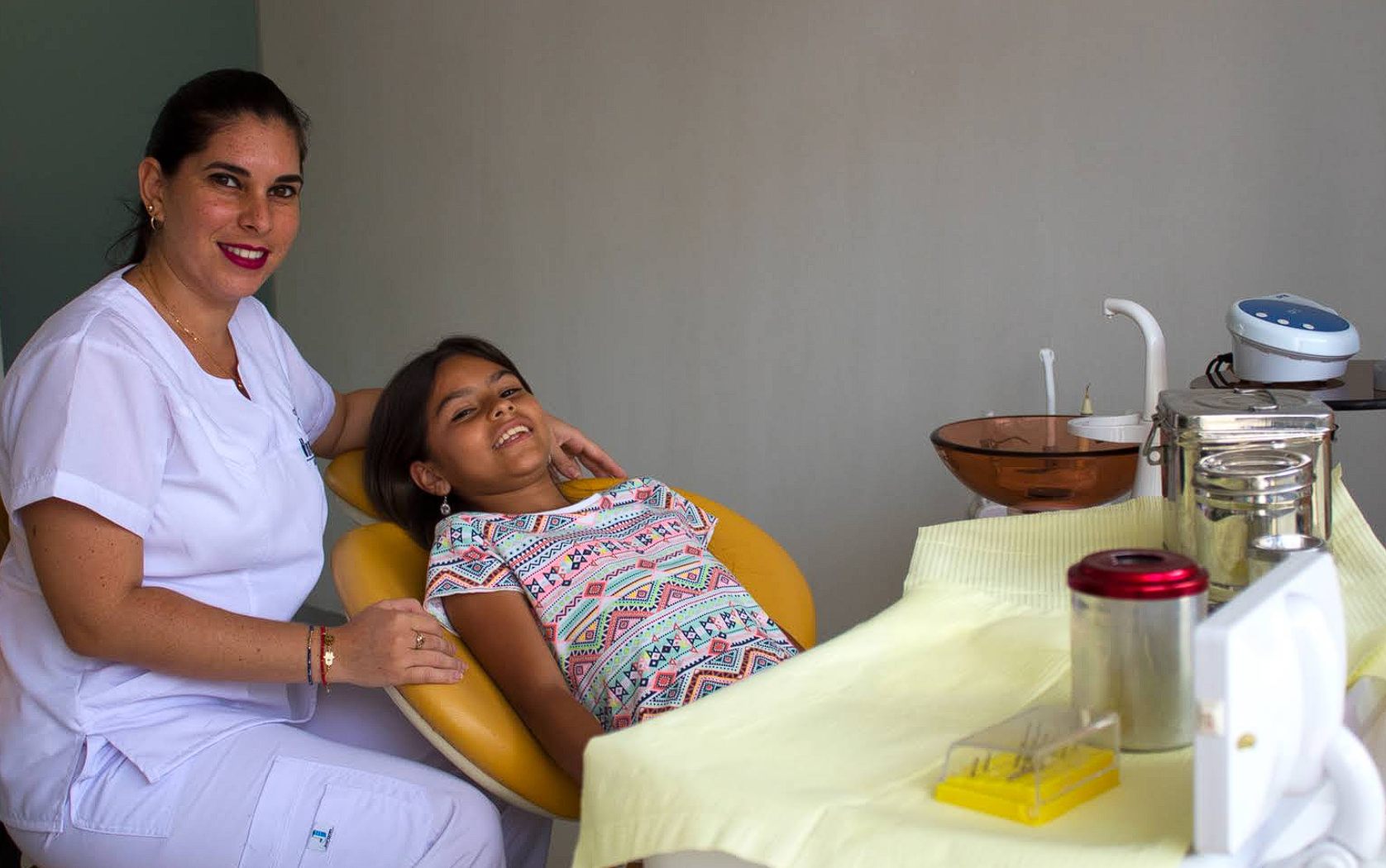 Odontóloga sonriendo junto a una niña en el sillón dental